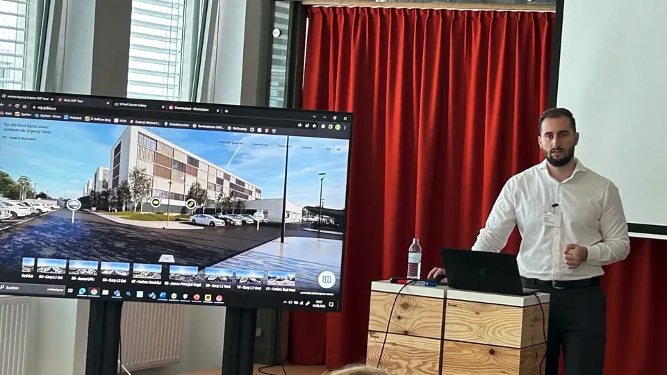 Ersan demonstrating a Virtual Spaces tour beside a large screen.